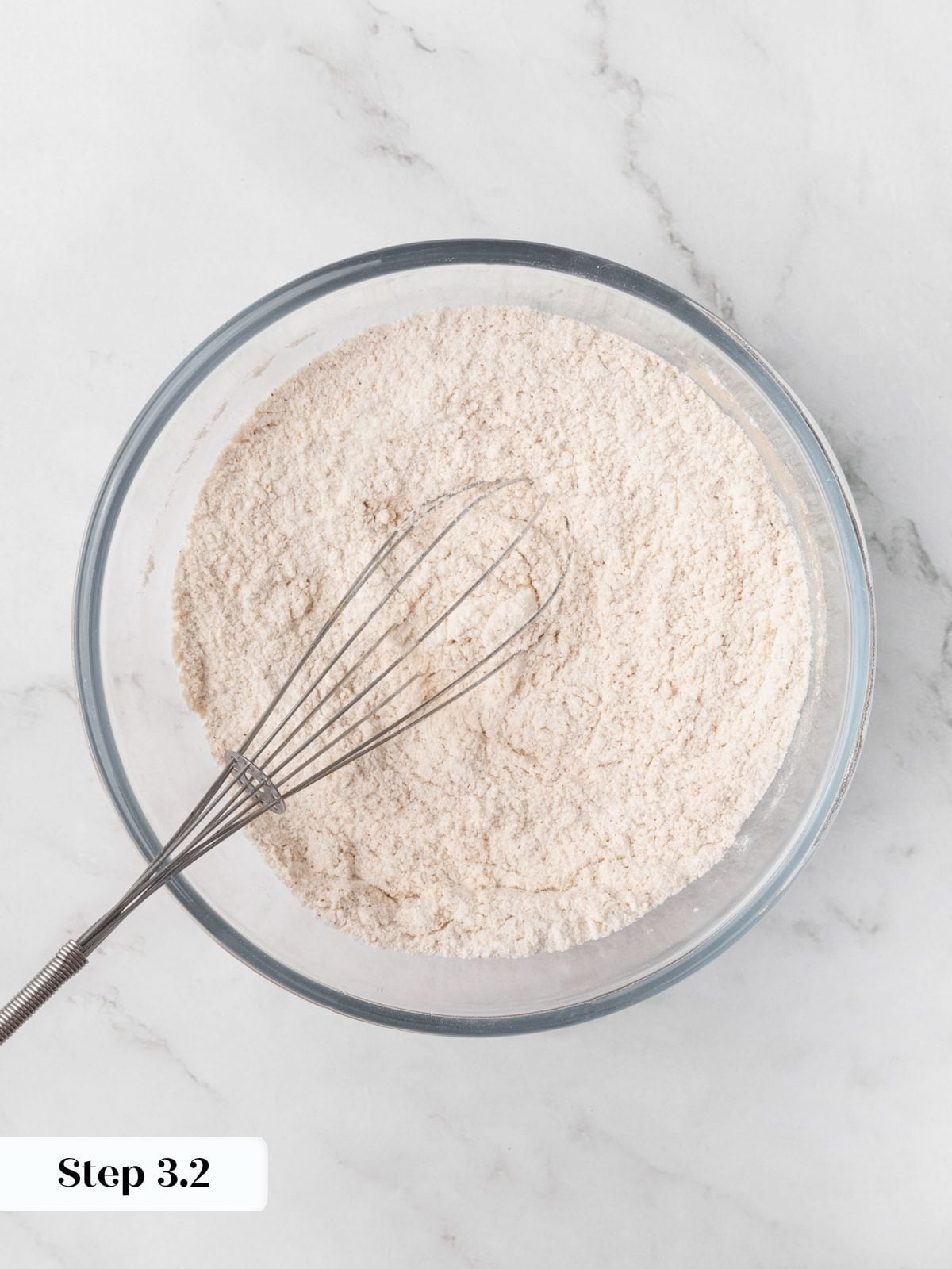 Pale tan dry mixture flecked with cinnamon evenly whisked together in a clear glass bowl.