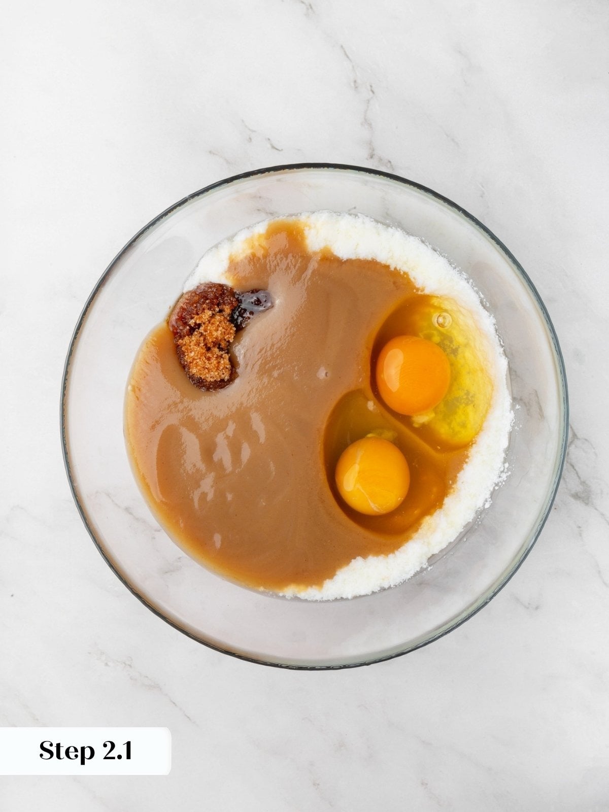 Eggs, applesauce, and brown sugar pooled together in a glass bowl ringed with granulated sugar.