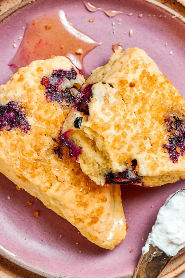 Two blueberry scones plated together with tender crumb visible and clotted cream tucked beneath them.