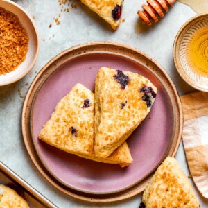 Two blueberry scones on a pink plate with raw sugar and honey bowl tucked alongside.
