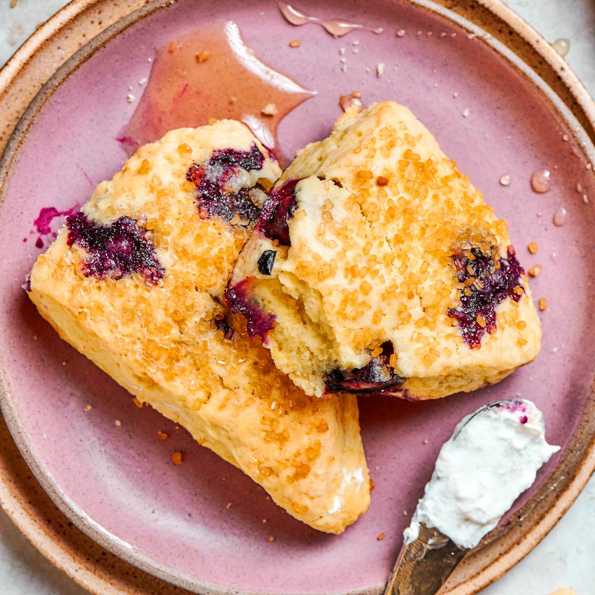 Two blueberry scones plated together with tender crumb visible and clotted cream tucked beneath them.