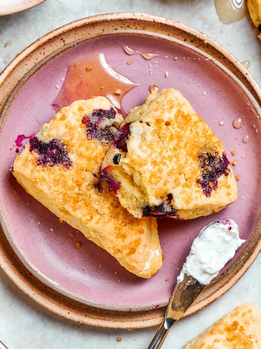 Blueberry scones on a pink ceramic plate, one tilted forward to reveal the tender crumb inside.