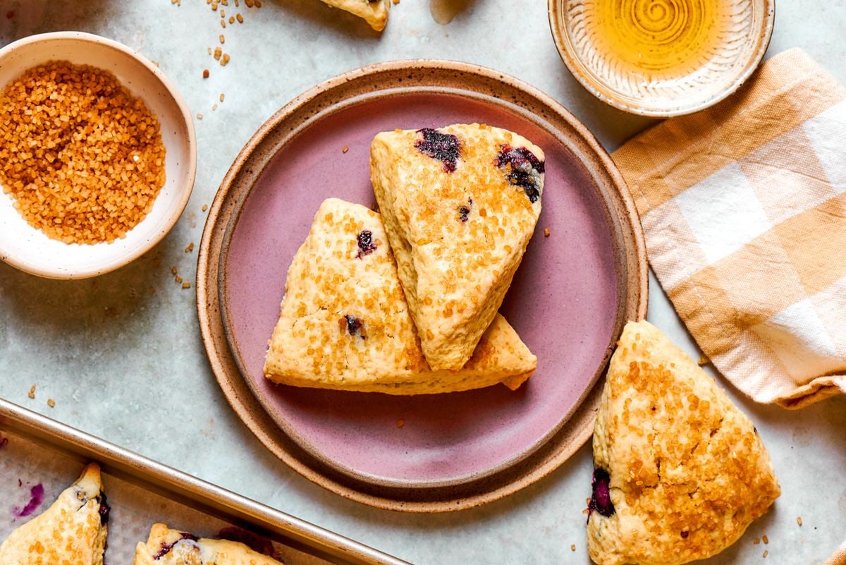 A tea-time moment of warm blueberry scones styled with raw sugar and a honey dipper nearby.