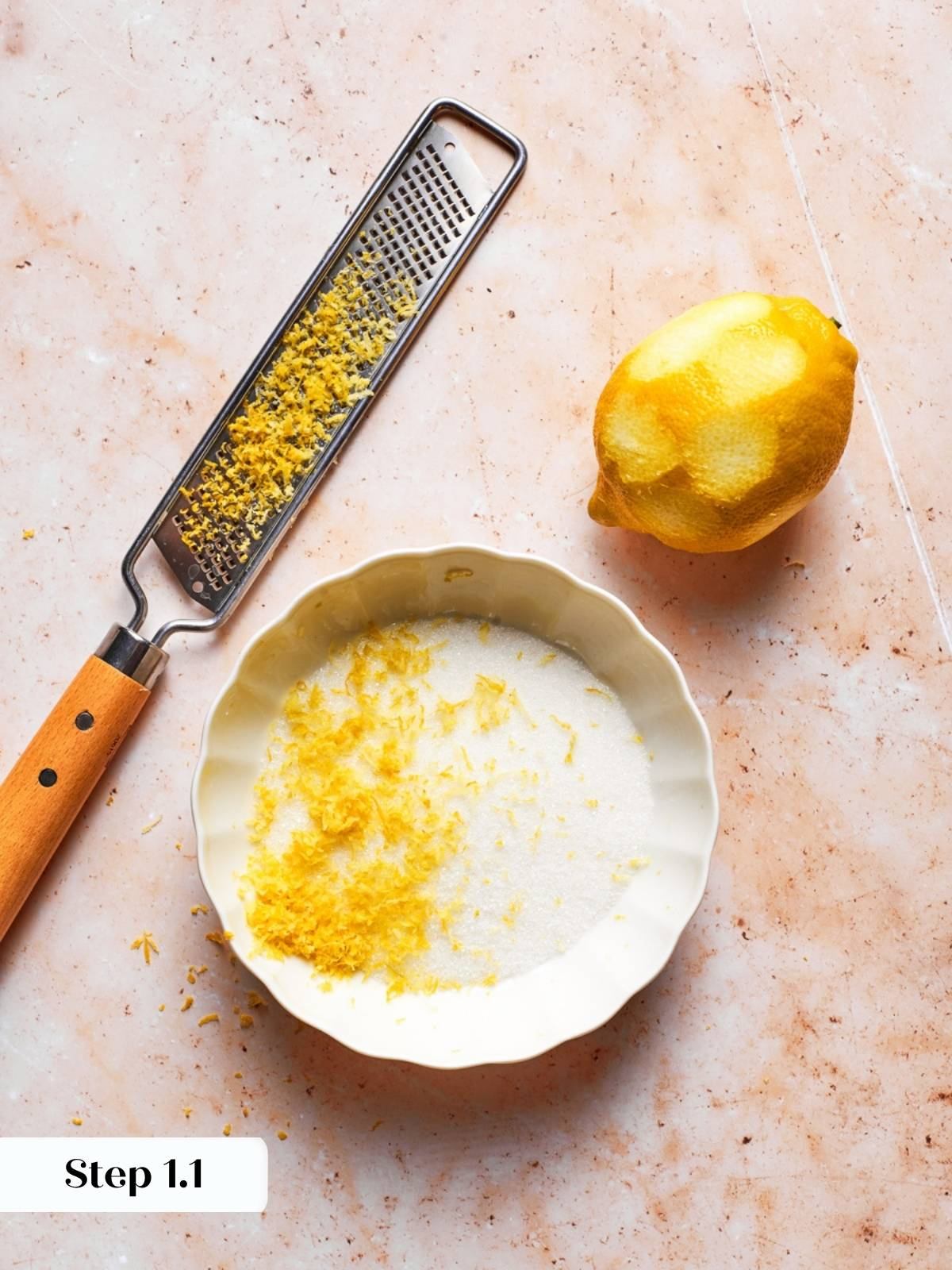 Lemon being zested onto granulated sugar in a fluted dish for blueberry scones recipe preparation.