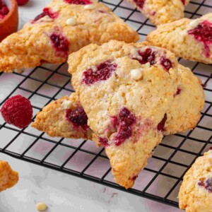Single raspberry white chocolate scone leaning forward showing juicy raspberry pockets and sparkling sugar topping.