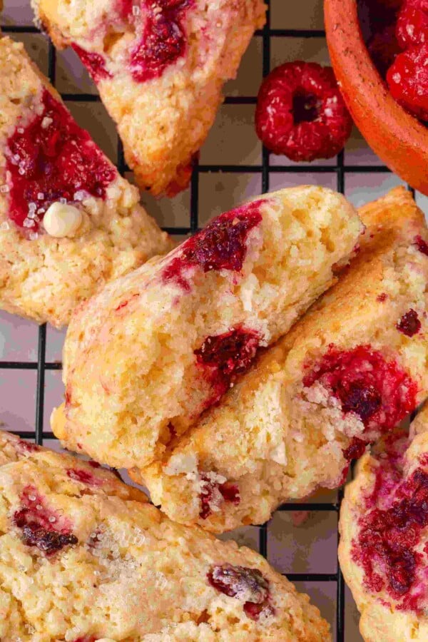 Split raspberry white chocolate scone on a wire rack with a terracotta bowl of frozen raspberries.