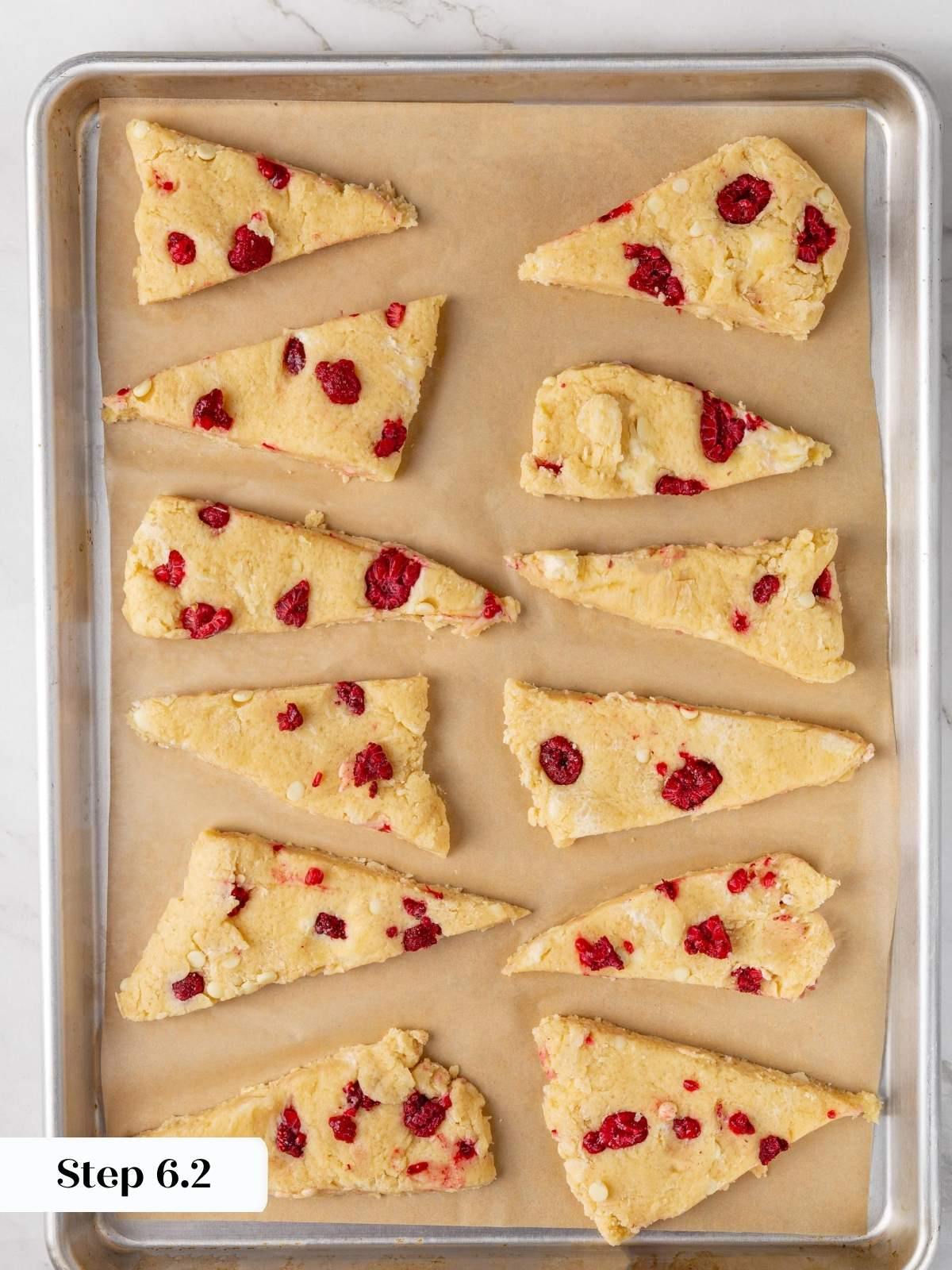 Twelve unbaked scone triangles arranged with space between them on a parchment-lined baking sheet before baking.