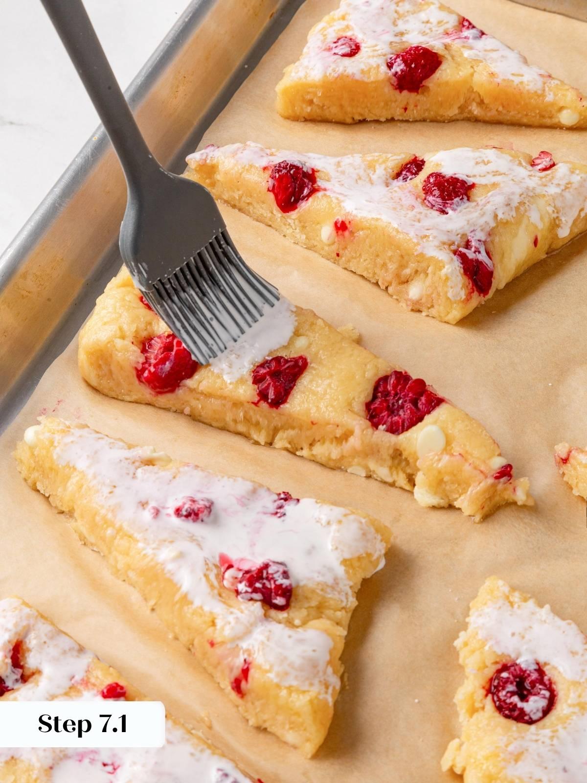 Pastry brush applying heavy cream wash to an unbaked scone on a parchment-lined baking sheet.