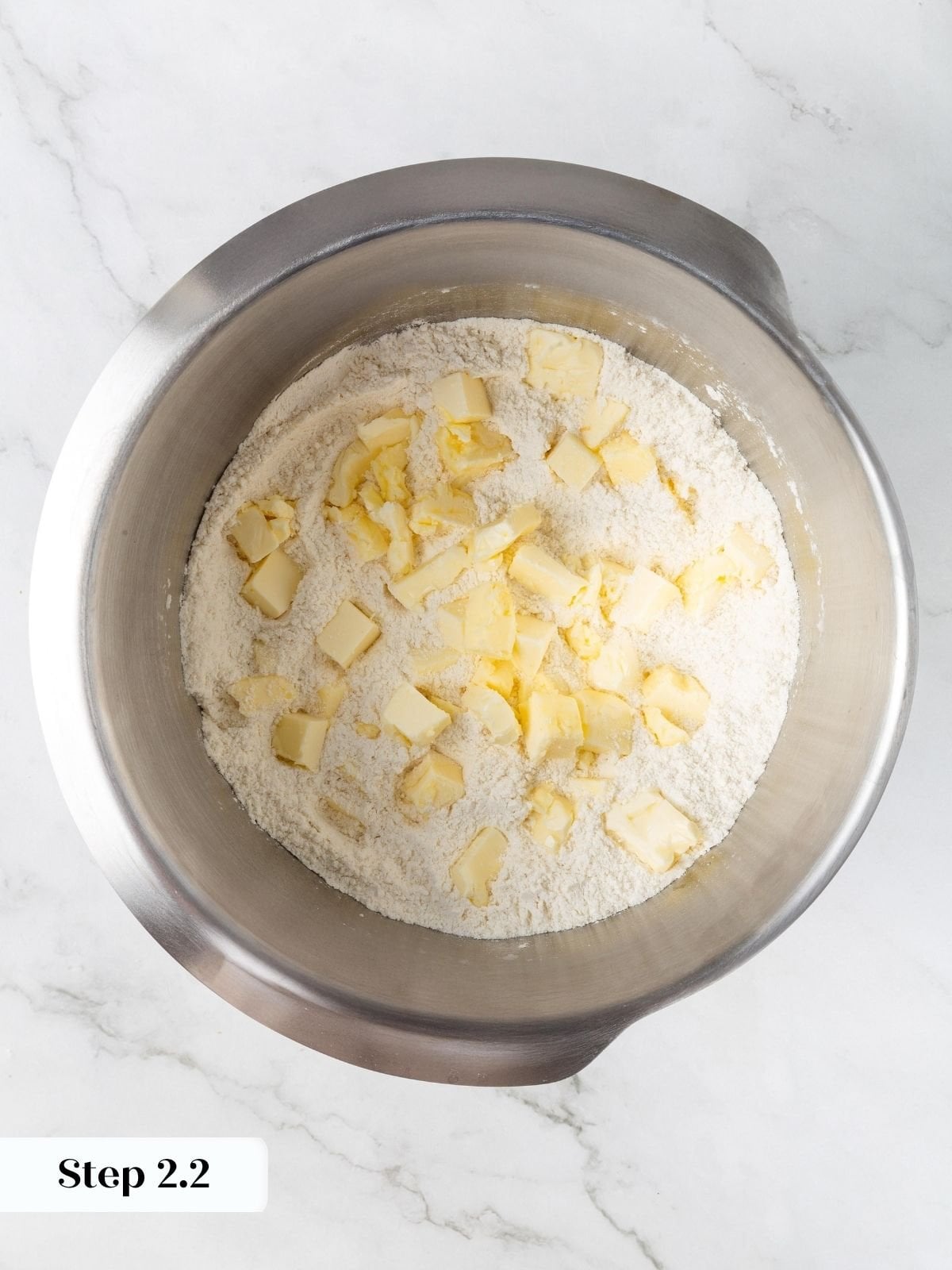 Cubed cold butter pieces scattered over dry flour mixture in a stainless steel stand mixer bowl.