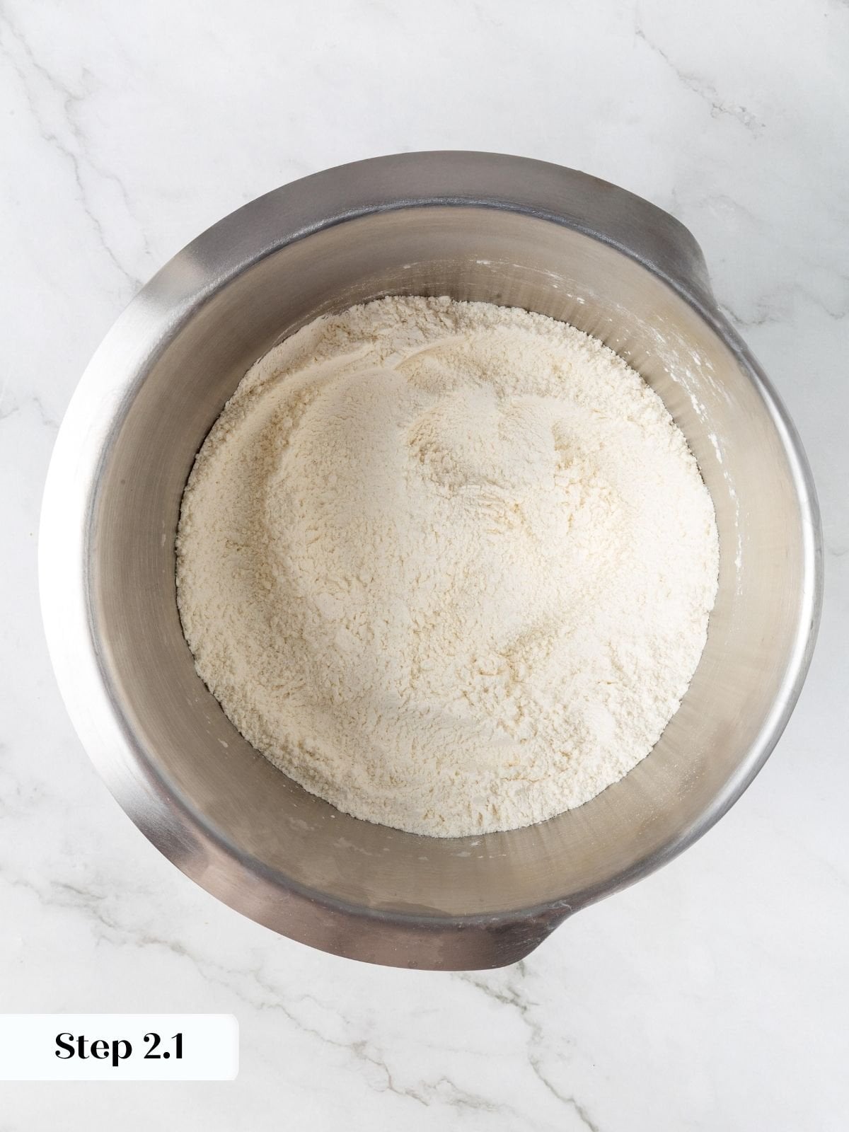 Flour, sugar, salt, and baking powder combined in a stainless steel stand mixer bowl on marble.