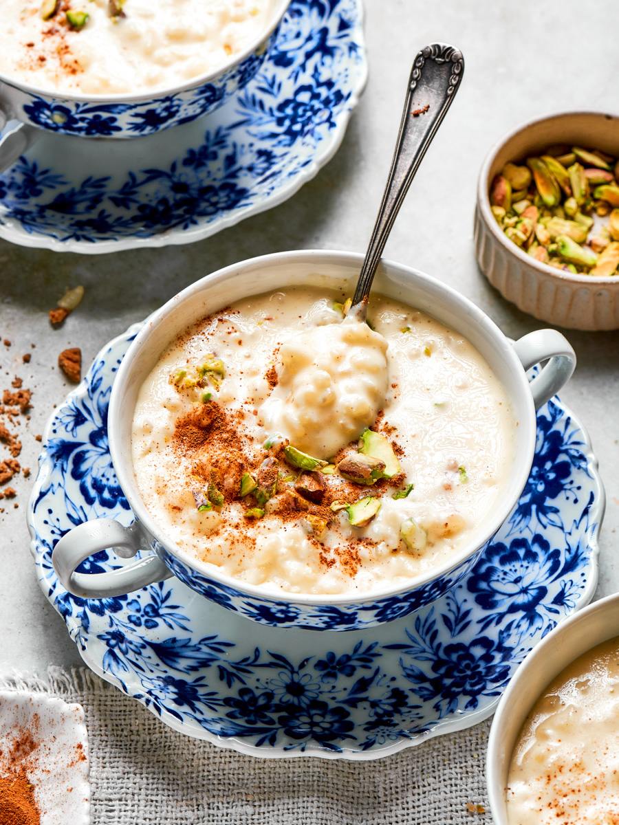 Spoon dipping into a bowl of rice pudding recipe with pistachios and cinnamon mid-serve.