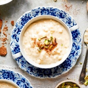 Creamy rice pudding recipe served in a blue floral bowl topped with chopped pistachios and cinnamon.