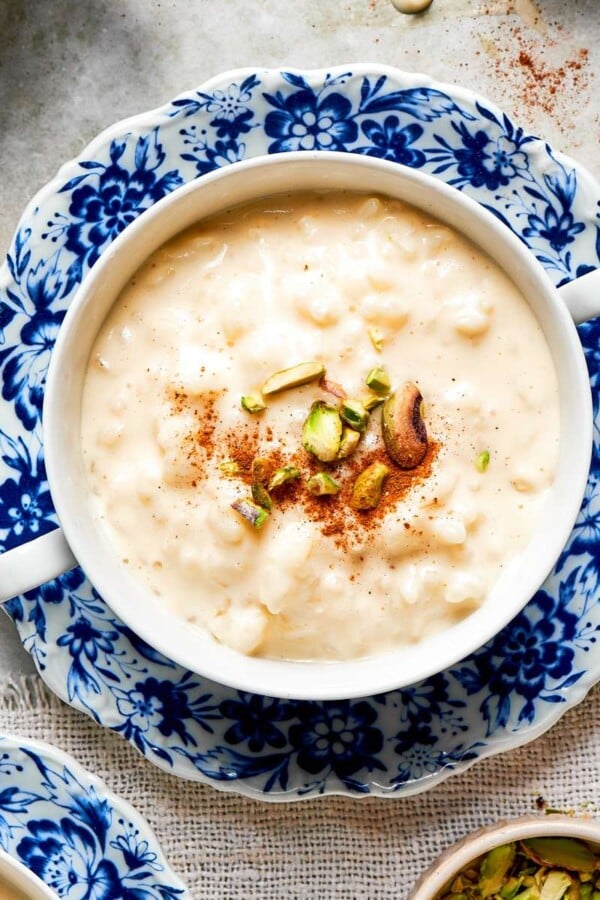 Creamy rice pudding recipe served in a blue floral bowl topped with chopped pistachios and cinnamon.