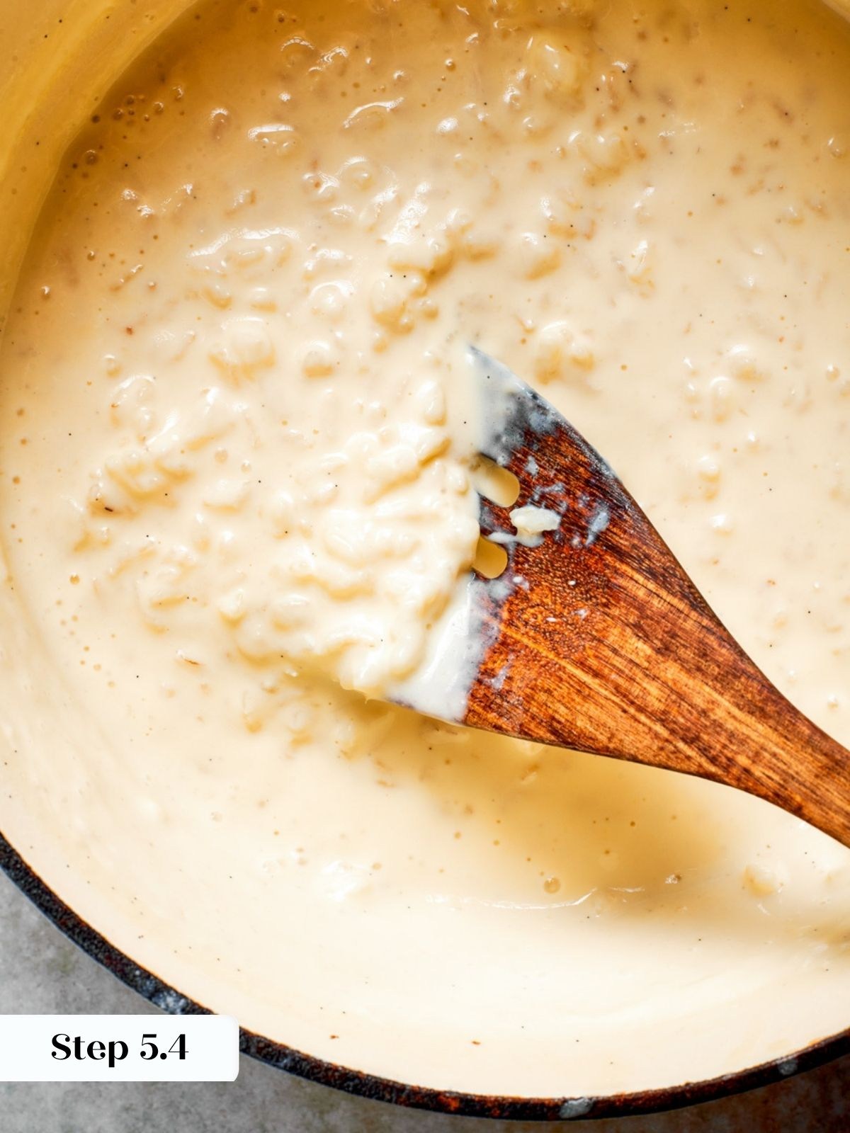 Wooden spatula coated thickly with creamy pudding, the doneness cue for this rice pudding recipe.
