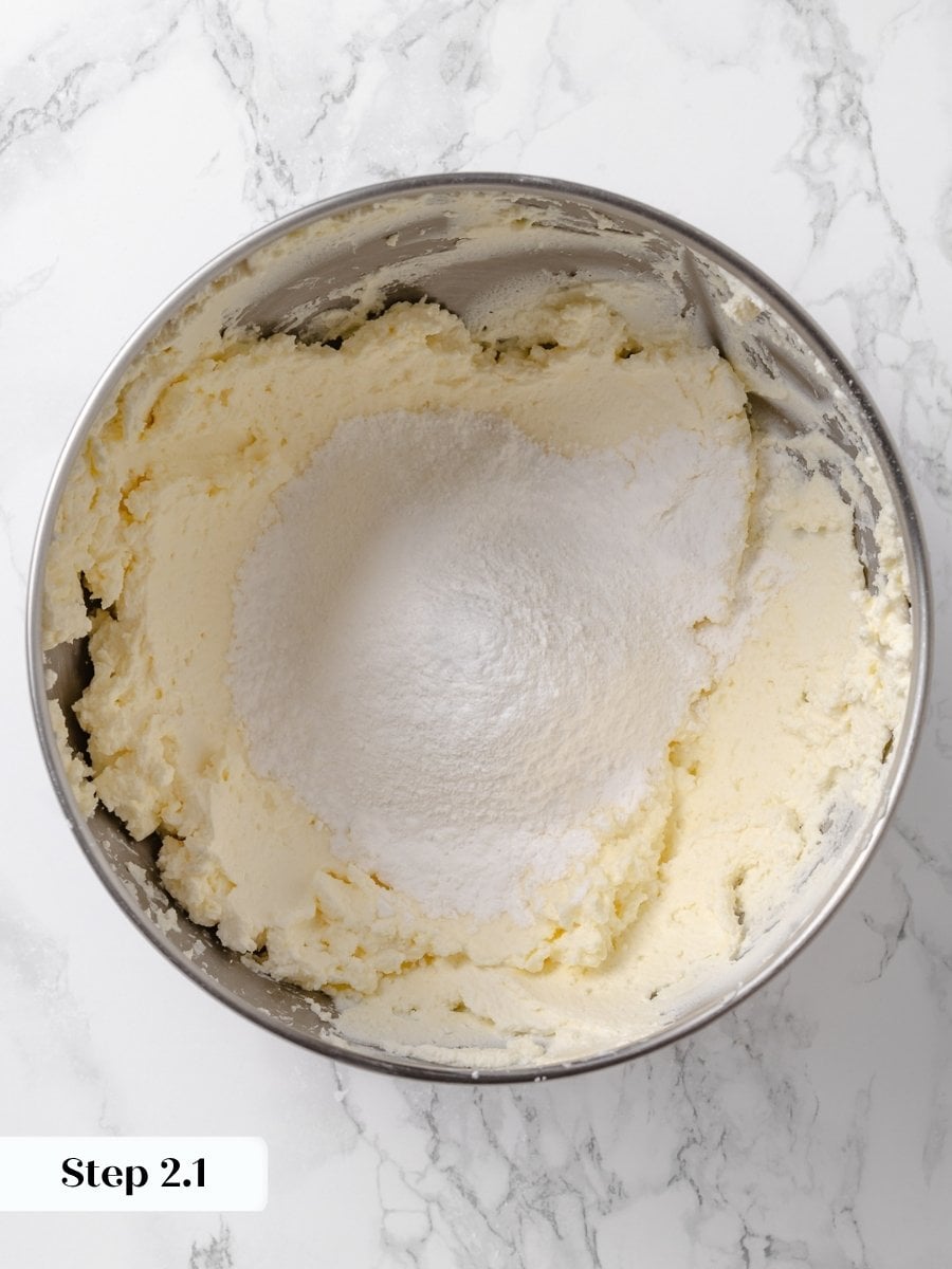 Powdered sugar mounded on top of beaten butter and cream cheese in a mixing bowl.