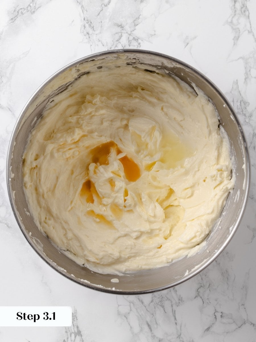 Lemon juice and vanilla extract added to cream cheese buttercream in a mixing bowl.