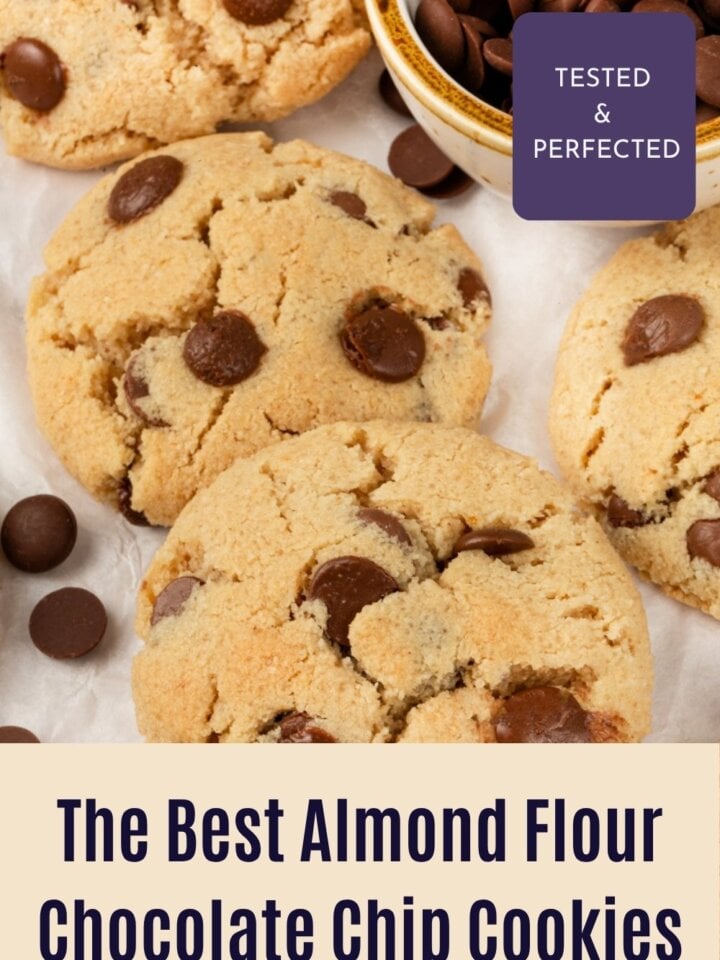 Almond flour chocolate chip cookies on parchment beside a bowl of chocolate chips, one cookie showing melty chocolate