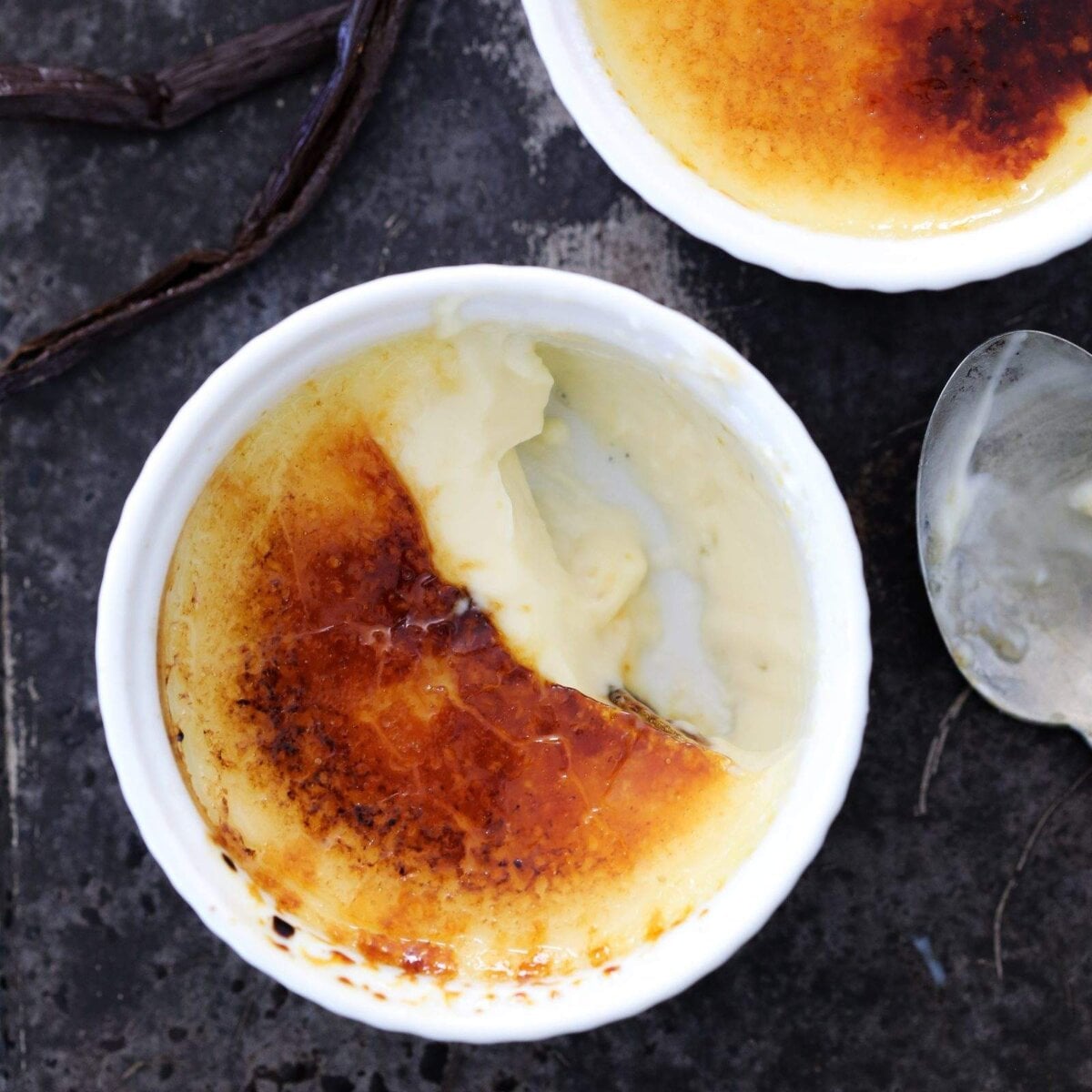 Whole vanilla pods beside the dish hint at the flecked custard inside this vanilla creme brulee.